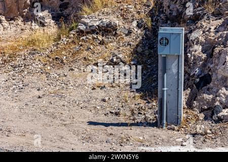 Base in calcestruzzo, tubo in plastica con cavi, scatola in metallo per misuratore elettrico, senza misuratore per presa di corrente, accanto a una collina rocciosa con erba selvatica asciutta su un Foto Stock