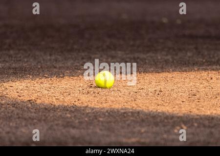 Softball giallo ottico su lanciatori di argilla circolare con erba sintetica marrone Foto Stock