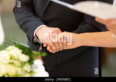il primo piano delle mani di una coppia di sposi stretti insieme simboleggia la loro unità e il loro impegno nel giorno del loro matrimonio Foto Stock