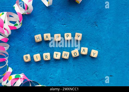 Biglietto di auguri di buon compleanno con blocchi di lettere in legno e serpentina su sfondo blu Foto Stock