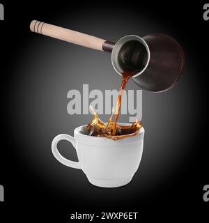 Versare caffè aromatico appena estratto dalla pentola turca nella tazza. Oggetti in aria su sfondo nero Foto Stock