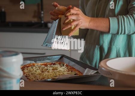 La donna sta grattugiando il formaggio sulla salsa di pomodoro fatta in casa con l'impasto della pizza spalmato in una padella. Pizza fatta in casa preparata per essere cotta a casa Foto Stock