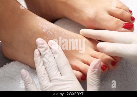 Pedicurista che applica la crema sul piede del cliente dopo la procedura di pedicure in salone di bellezza, primo piano Foto Stock