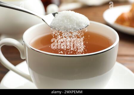 Aggiungere zucchero nella tazza di tè a tavola, primo piano Foto Stock