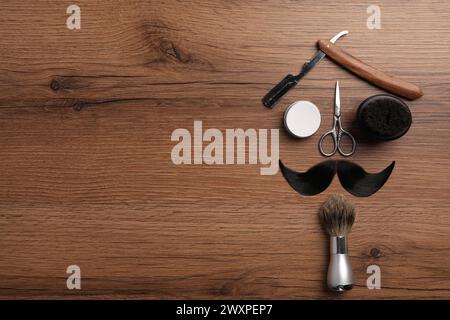 Baffi artificiali e utensili da barbiere su tavola di legno, posate in piano. Spazio per il testo Foto Stock