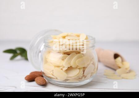 Fiocchi di mandorle fresche in vaso e noci su un tavolo bianco testurizzato, primo piano Foto Stock