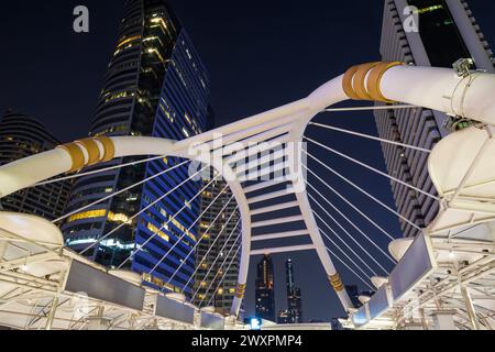 Chong Nonsi Skywalk - passerella pedonale illuminata, arco del ponte - e grattacieli nel centro di Bangkok, Thailandia, al crepuscolo. Foto Stock