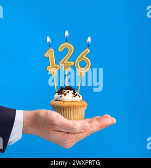 Cupcake per il compleanno a mano - candela numero 126 su sfondo blu Foto Stock