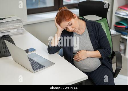 Donna incinta che dorme alla sua scrivania in ufficio. Foto Stock