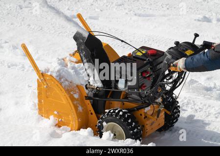 Lavoratore che utilizza una macchina spazzaneve per rimuovere la neve dal parcheggio dopo un uragano invernale. Rimozione meccanizzata della neve dal marciapiede, pulizia dell'area nelle giornate di sole Foto Stock