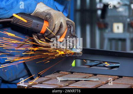 Locksmith in occhiali speciali lavora nella lavorazione dei metalli di produzione con scintille emesse da una smerigliatrice angolare Foto Stock