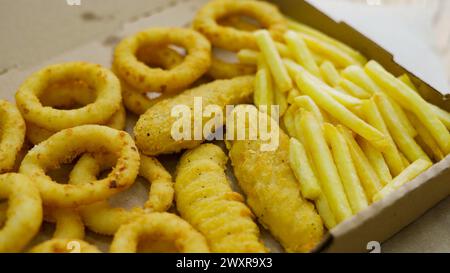 Set di scatole di carta da asporto con diversi fast food, patatine fritte, pepite, anelli di cipolla e diverse salse Foto Stock