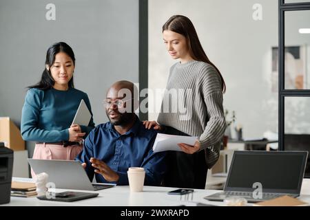 Foto di gruppo medio-lungo di tre uomini e donne etnie diverse che collaborano a progetti aziendali in un ufficio moderno, spazio di copia Foto Stock