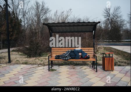 un anziano senzatetto giace a dormire su una panchina del parco in autunno Foto Stock