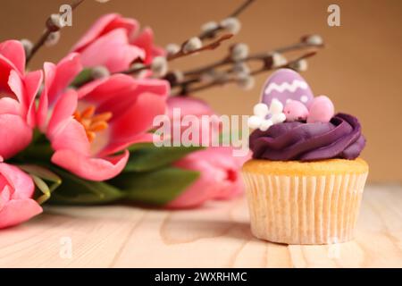 Delizioso cupcake pasquale decorato, fiori e rami di salice su un tavolo di legno Foto Stock