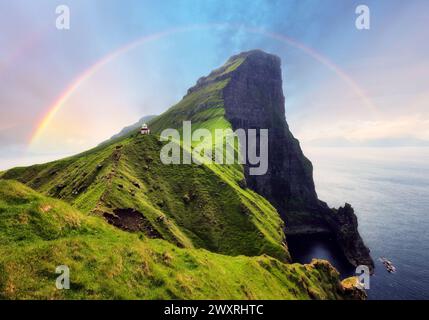 Isola di Faroe in Danimarca con arcobaleno - Faro di Kallur sulle verdi colline dell'isola di Kalsoy al tramonto, fotografie di paesaggi Foto Stock