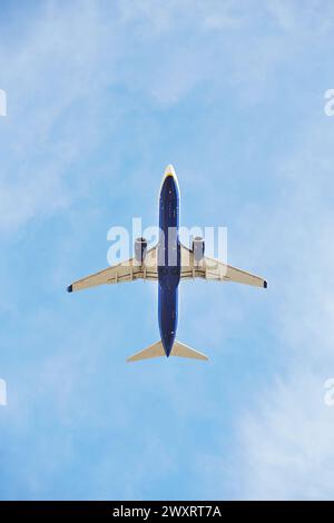 Aereo commerciale catturato dal basso mentre si arrampica nel vasto cielo blu, mostrando il suo ventre e i motori jet Foto Stock