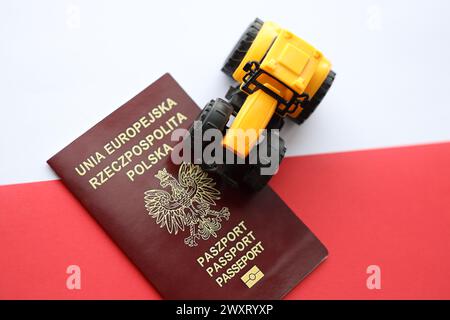 Passaporto rosso polacco e trattore giallo su una bandiera bianca e rossa liscia della Polonia Foto Stock