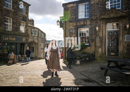 Haworth, West Yorkshire, Regno Unito. Visitatori in cima a Main Street in una giornata di sole primaverili. Foto Stock