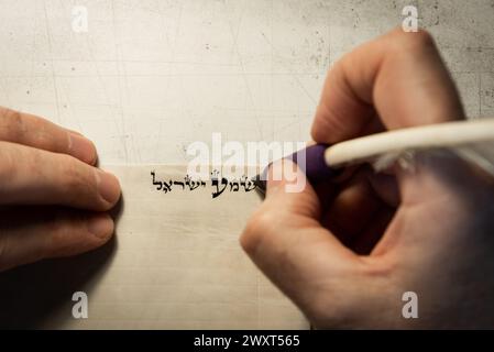 Vista ravvicinata delle mani di uno scriba ebreo che scrive le parole della preghiera di Shemà Israele su pergamena che sarà racchiusa in una mezuzah e posta o Foto Stock