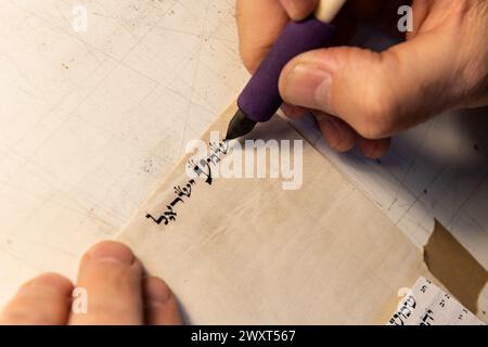 Vista ravvicinata delle mani di uno scriba ebreo che scrive le parole della preghiera di Shemà Israele su pergamena che sarà racchiusa in una mezuzah e posta o Foto Stock