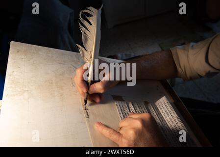 Vista ravvicinata delle mani di uno scriba ebreo che tiene una trappola di piume e scrive le parole della preghiera di Shema Yisrael sulla pergamena che sarà encas Foto Stock