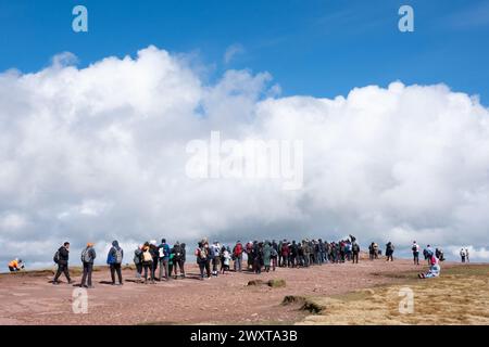 Brecon Beacons, Galles. Una fila di camminatori e scalatori fa la fila per scattare una foto dal punto di trig in cima alla Pen Y fan. Il punto più alto dei Brecons Foto Stock