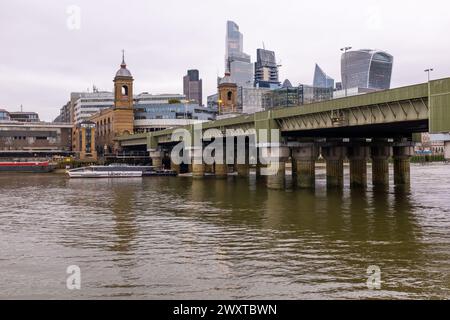 Una barca Uber sul fiume Tamigi scivola sotto il ponte ferroviario di Cannon Street con la stazione di Cannon Street e i grattacieli della città alle spalle. Foto Stock