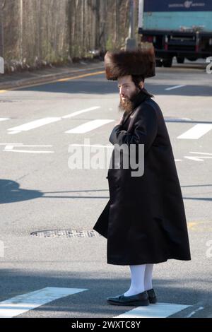 Su Purim, un ebreo ortodosso con un cappello in pelliccia di shtreimel e calzini alti, attraversa una strada a Brooklyn, New York. Foto Stock