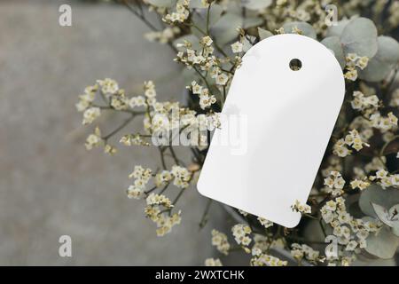 Matrimonio floreale, mockup di compleanno. Etichetta regalo in carta vuota, etichetta. Fiori di Limonio e rami di alberi di eucalipto bouquet in secchio di metallo. Sfocato Foto Stock