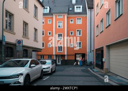 Un veicolo bianco è parcheggiato in un vicolo stretto tra due edifici arancioni. La sua illuminazione automobilistica risplende negli spazi ristretti Foto Stock