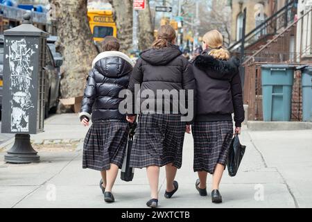Tre ragazze ebree ortodosse in gonne identiche camminano a stretto contatto a Brooklyn, New York. Sono compagni di classe nelle uniformi scolastiche. Foto Stock