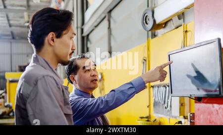 Due uomini che conversano accanto a un computer in fabbrica Foto Stock