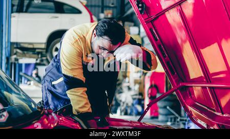 Uomo in giallo e nero che lavora su un'auto rossa Foto Stock