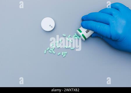 Primo piano delle mani di un operatore medico o farmacista in guanti protettivi in lattice blu che versano pillole su una superficie di colore blu Foto Stock