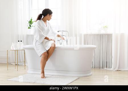 Donna che si prepara per un bagno in una stanza luminosa Foto Stock