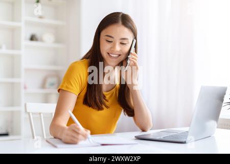 Donna al telefono che scrive appunti con il portatile aperto Foto Stock