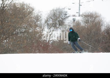 Uno sciatore che scivola giù per una pista innevata vicino agli alberi e agli impianti di risalita Foto Stock
