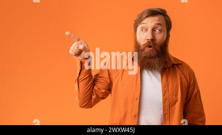 Sorpreso Bearded Redhaired Guy che punta da parte con il suo Finger, Studio Foto Stock