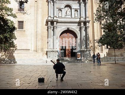 Un chitarrista spagnolo classico si staglia in autobus illuminati dalla luce del sole in una piazza di fronte alla cattedrale di Granada, Andalusia, Spagna Foto Stock