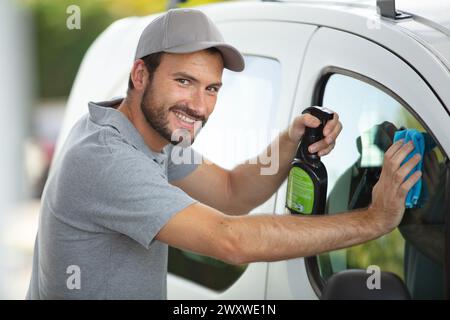 man spruzza lo shampoo per auto sul finestrino dalla bottiglia di plastica Foto Stock