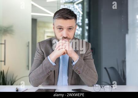Un uomo d'affari professionista con una tuta si impegna in una seria conversazione di videochiamata, illustrando comunicazioni remote e discussioni aziendali. Foto Stock