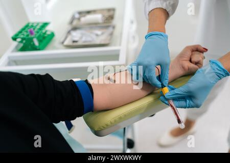 Primo piano di lavoratrice di laboratorio in guanti medici blu che raccolgono campioni di sangue o campioni da vena paziente in laboratorio medico, flusso di sangue Foto Stock