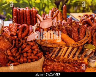 Diversi tipi di salsicce a secco affumicate fatte in casa appese su uno sfondo di legno scuro. Assortimento di deliziosi salumi, salumi e peperoni. carne per Foto Stock