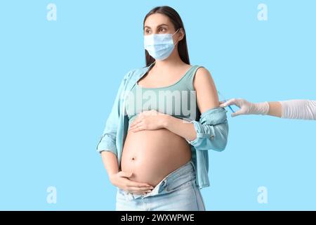 Giovane donna incinta in maschera medica che riceve il vaccino su sfondo blu Foto Stock