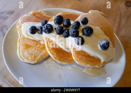 Focalizzazione superficiale sui mirtilli conditi con miele su uno yogurt cremoso e tre pancake spessi Foto Stock