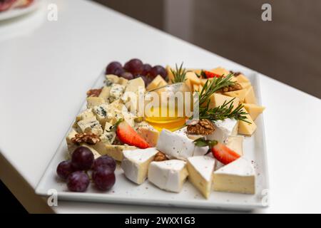 Piatto di formaggi con frutta e spezie su un tavolo bianco. Formaggi diversi su piatto in ceramica bianca. Foto Stock