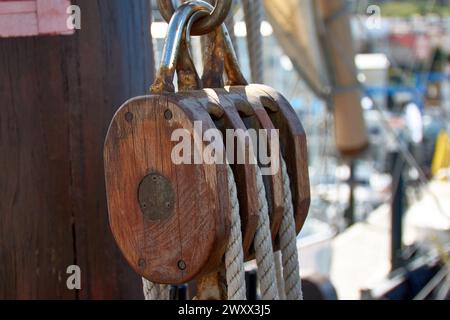 Carrucola per vele e corde in legno sulla replica della caravella di Santa Maria, con la vela e altre navi nel porto, morbida e fuori fuoco Foto Stock