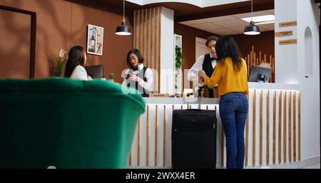 Il personale della reception assiste le donne nella procedura di registrazione, chiedendo di vedere il passaporto e firmare i documenti di conferma per la sistemazione. Due ospiti che arrivano al rifugio vacanze a cinque stelle. Foto Stock