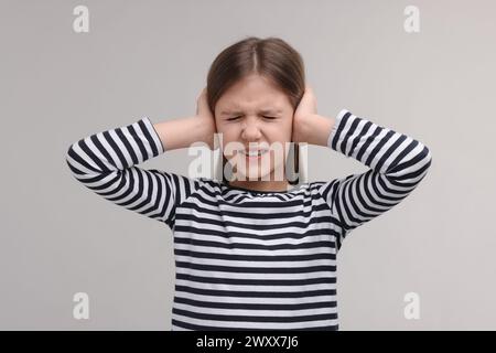 Problemi di udito. Bambina che soffre di dolore alle orecchie su sfondo grigio Foto Stock